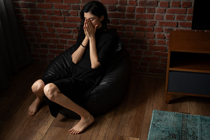 Woman showing signs of being too depressed to babysit, sitting on a black bean bag chair in a dimly lit room. Woman showing signs of being too depressed to babysit, sitting on a black bean bag chair in a dimly lit room.