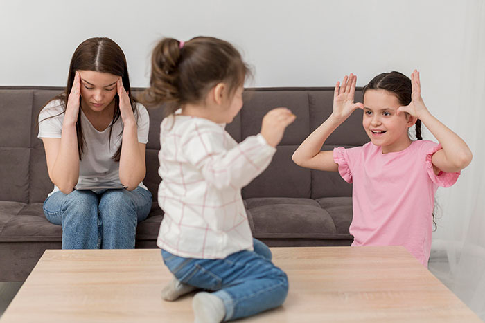 Woman looking overwhelmed and depressed babysitting two energetic children playing on a couch and table indoors. Woman looking overwhelmed and depressed babysitting two energetic children playing on a couch and table indoors.