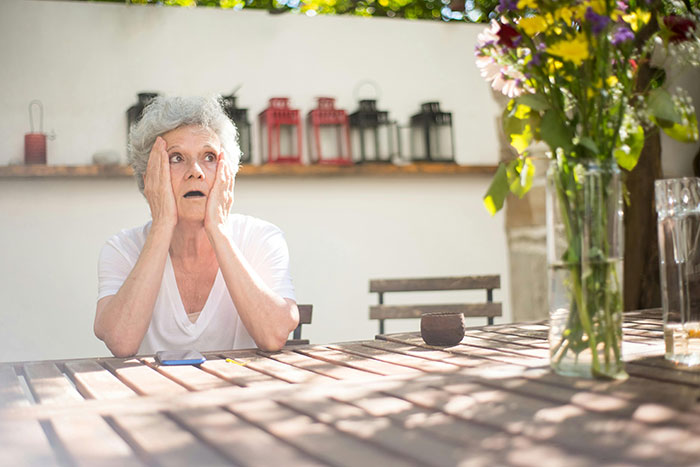 Elderly woman sitting at a wooden table outdoors looking shocked, reflecting the couple goes ballistic wedding dispute. Elderly woman sitting at a wooden table outdoors looking shocked, reflecting the couple goes ballistic wedding dispute.