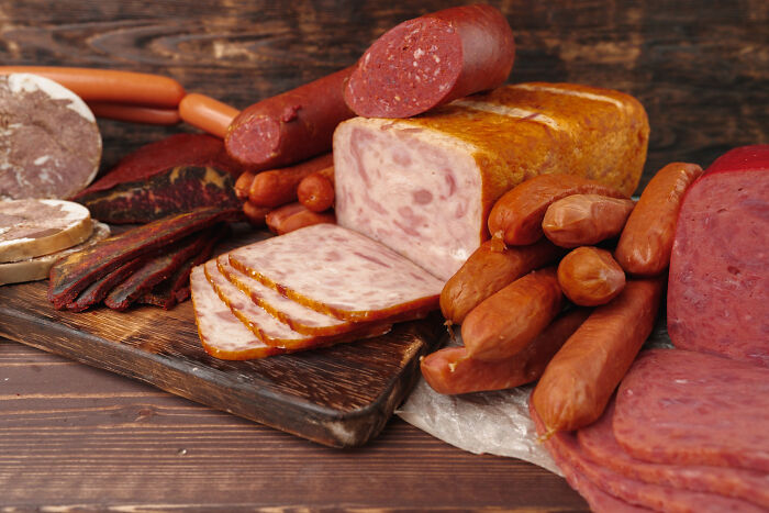 Assorted processed meats displayed on a wooden board highlighting products requiring extra caution while cooking and eating.
