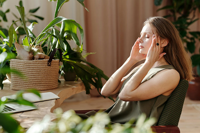 Woman sitting at desk surrounded by plants, appearing stressed, reflecting on couple and bully bro wedding conflict. Woman sitting at desk surrounded by plants, appearing stressed, reflecting on couple and bully bro wedding conflict.