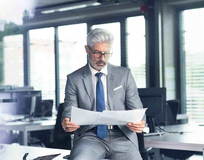 Businessman in a gray suit and glasses reading documents in a modern office representing people in charge.