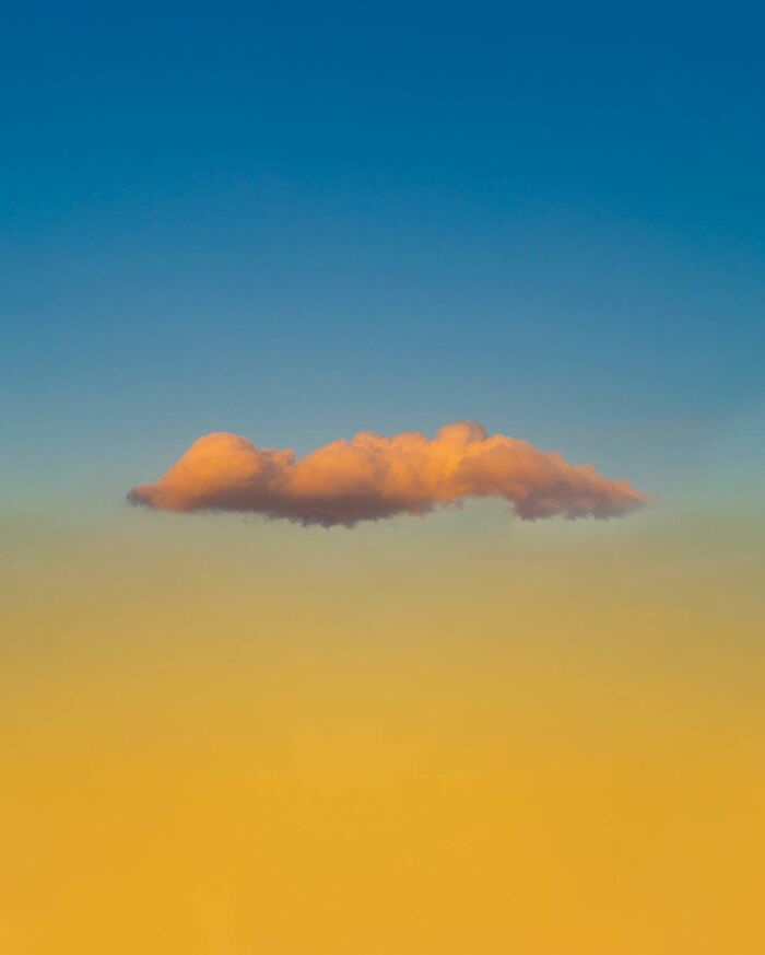 Single orange cloud floating in a vibrant blue and yellow sky, showcasing creative photo manipulations and surreal reality elements.