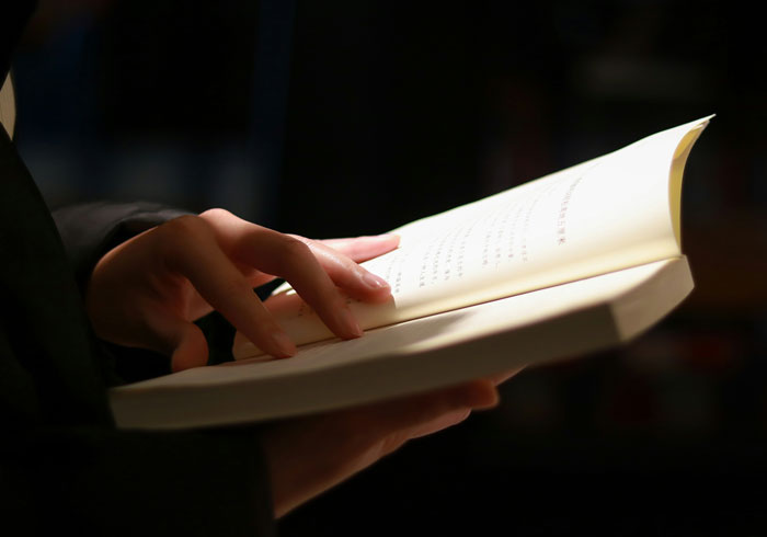 Person holding and reading a book under warm light illustrating 2025 summer reading list runs in newspapers. Person holding and reading a book under warm light illustrating 2025 summer reading list runs in newspapers.