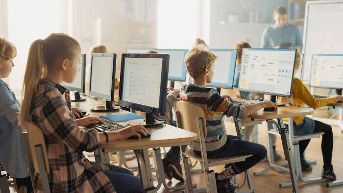 Students in a classroom working on computers while a teacher conducts a lesson about life blunders and secrets.