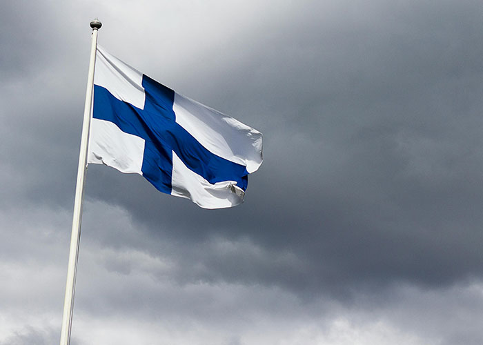 Finnish flag waving against dark clouds representing the best and worst things about living in home countries.