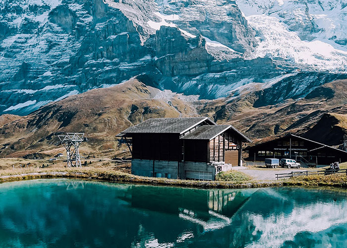 Scenic mountain landscape with wooden houses and a lake reflecting the snowy peaks, showcasing living in home countries.