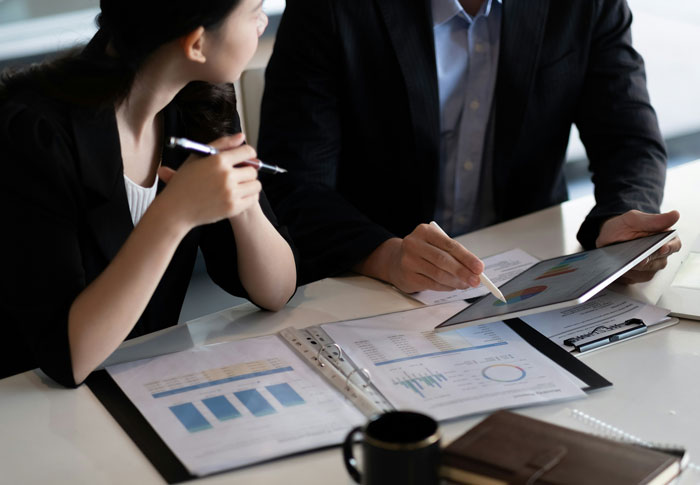 Two professionals reviewing charts and data on a tablet and documents during a business meeting about leadership.