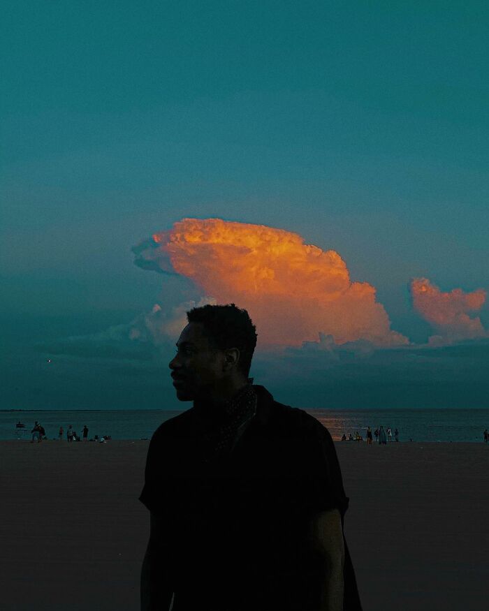 Silhouette of a man on the beach at dusk with vibrant orange clouds in a creative photo manipulation surreal reality scene.