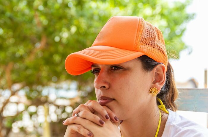 Woman wearing an orange cap, resting her chin on clasped hands, reflecting on a tiny thing that made trip better outdoors.