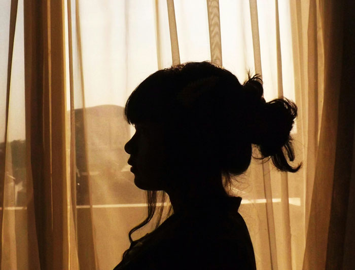 Silhouette of a woman by a window with curtains, representing secrets spouses keep after marriage.