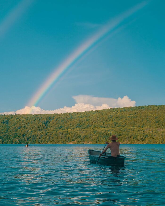 Person paddling a boat on a lake under a rainbow with creative photo manipulations inviting surreal reality.