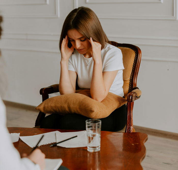 Young woman sitting with a pillow, holding her head in frustration, illustrating infuriating things said by people in charge.