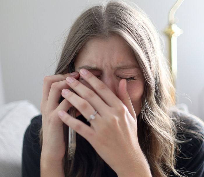 Woman covering face in distress while holding phone, illustrating conflict over obese mom babysitting newborn topic. Woman covering face in distress while holding phone, illustrating conflict over obese mom babysitting newborn topic.