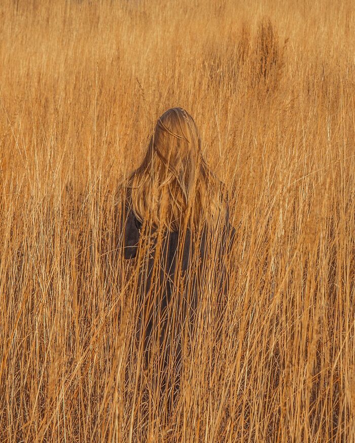 Woman with long hair standing in tall dry grass field, a creative photo manipulation evoking surreal reality.