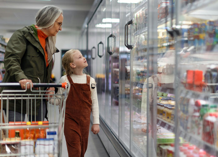 Older woman and child shopping together, exploring frozen foods aisle illustrating money saving habits that cost more.