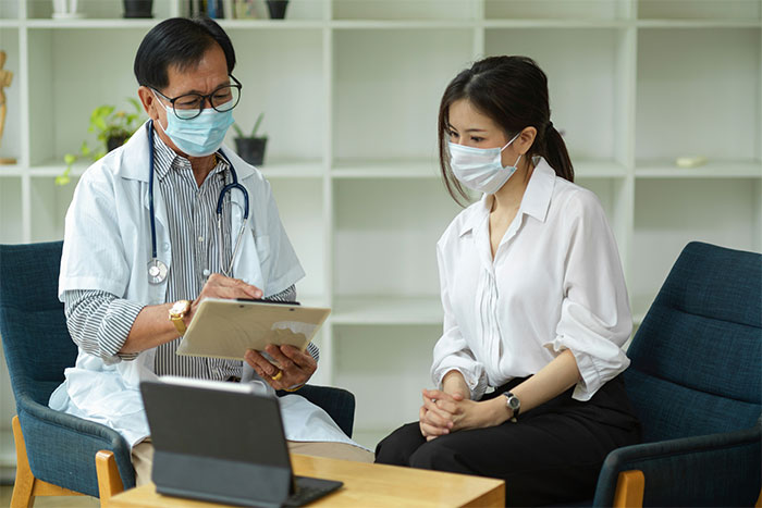 Doctor and woman wearing masks in office setting, discussing a severe case of attention seeking during consultation. Doctor and woman wearing masks in office setting, discussing a severe case of attention seeking during consultation.