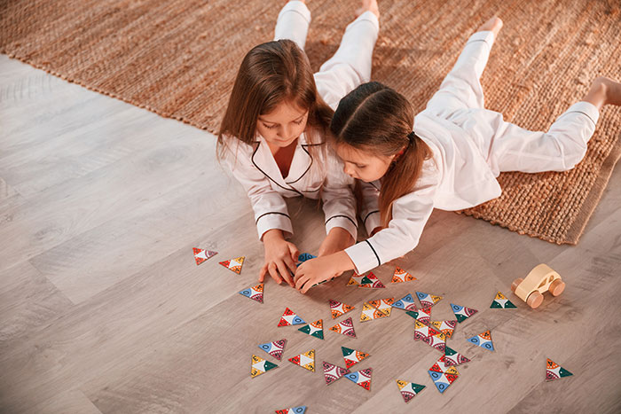 Two young girls in pajamas playing on the floor with toys, highlighting furniture damage and friend disputes. Two young girls in pajamas playing on the floor with toys, highlighting furniture damage and friend disputes.