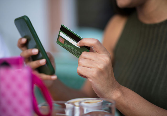 Person holding a credit card and phone, symbolizing secrets spouses keep about finances after marriage.