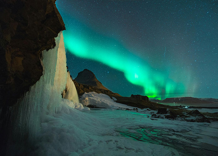 Frozen waterfall and northern lights over a mountain landscape revealing the best and worst things about living in home countries