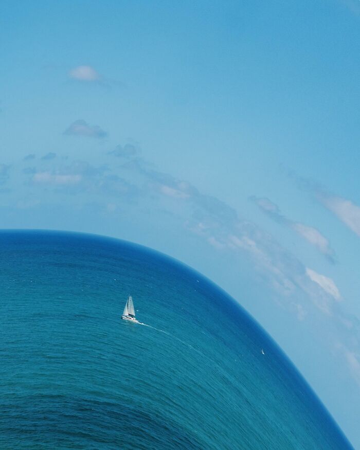 Sailboat on curved ocean blending into surreal sky created with creative photo manipulations.