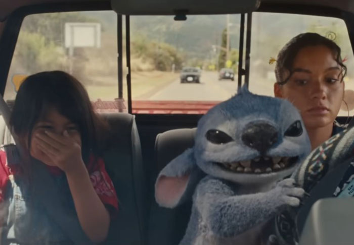 Lilo & Stitch live-action scene with Stitch character and two female passengers inside a moving car on a sunny day. Lilo & Stitch live-action scene with Stitch character and two female passengers inside a moving car on a sunny day.