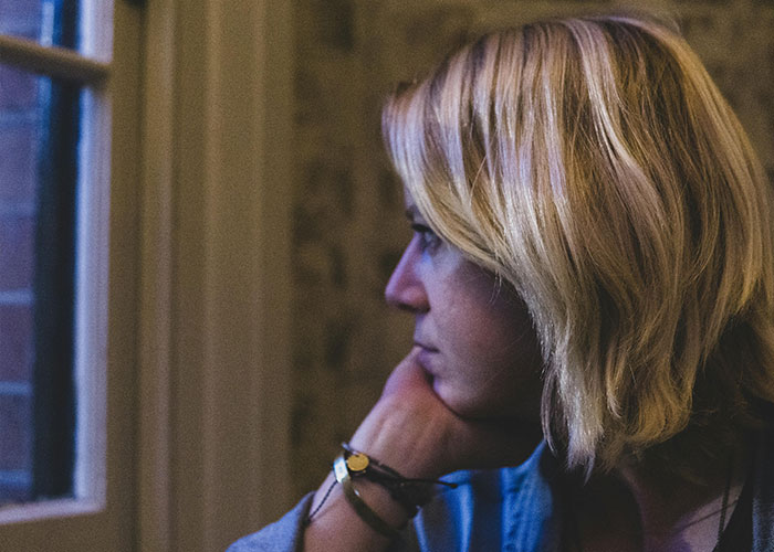 Woman with blonde hair looking thoughtfully out a window, reflecting on neighbor stealing packages and getting petty. Woman with blonde hair looking thoughtfully out a window, reflecting on neighbor stealing packages and getting petty.