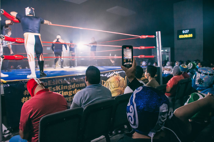 Audience at a wrestling match capturing moments on their phones, highlighting secrets spouses may keep after marriage.