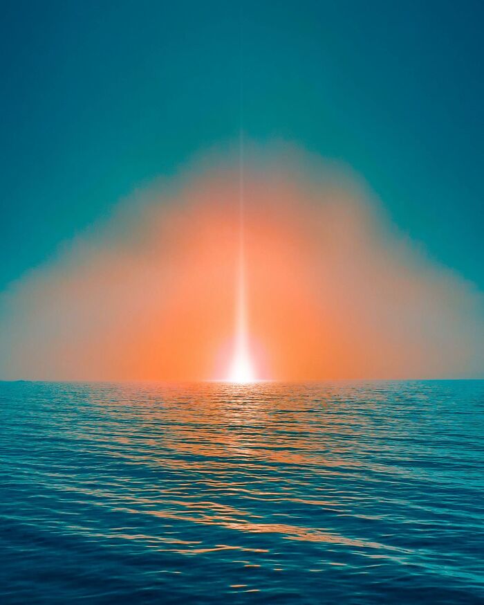 Surreal creative photo manipulation showing a glowing light rising from the ocean horizon against a vibrant sky.
