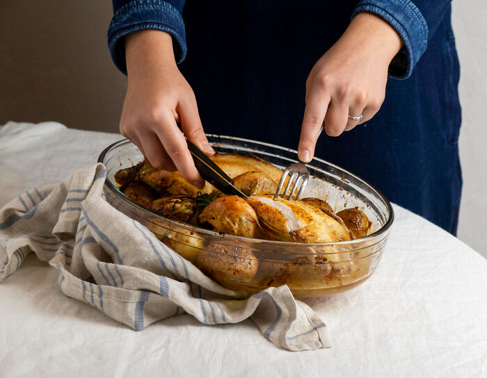 Person carving roasted chicken in glass dish, highlighting products requiring extra caution while cooking and eating