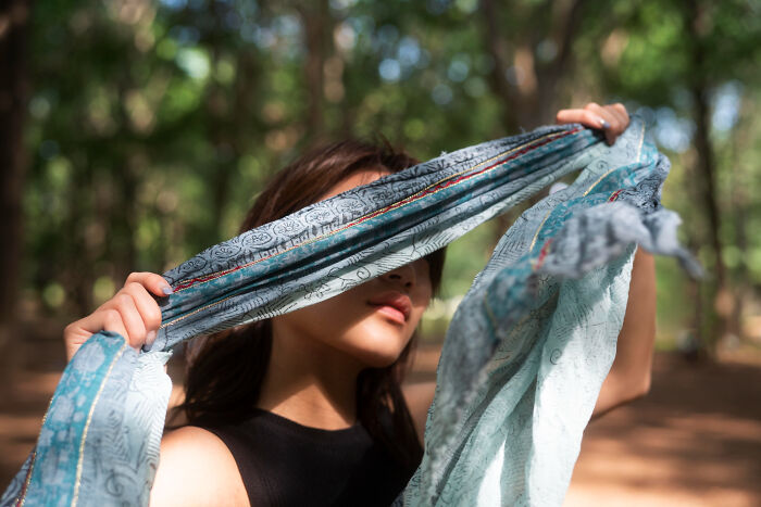 Young woman outdoors using a tiny thing made trip better by shielding her eyes with a patterned scarf in sunlight.