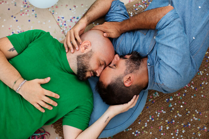 Two men lying close together on the floor, sharing an intimate moment surrounded by colorful confetti, capturing celebrity gossip vibes.
