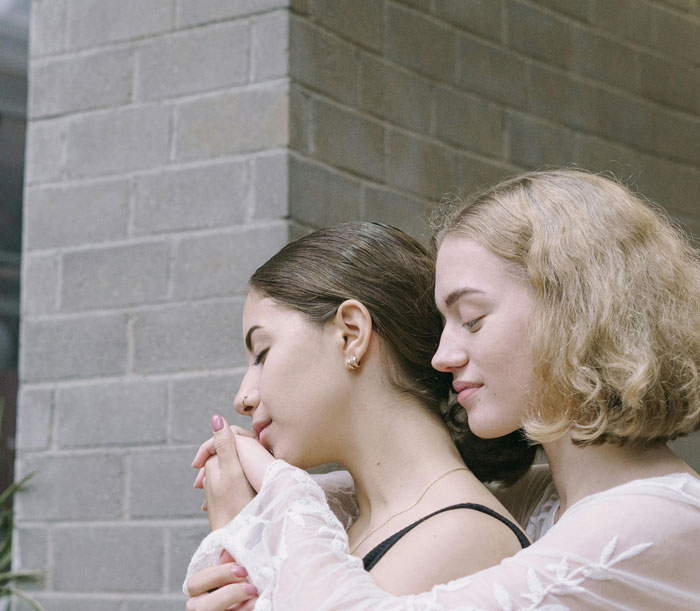 Two women embracing gently by a brick wall, reflecting on secrets spouses keep after marriage in a tender moment.