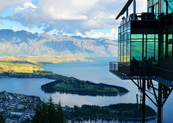 Scenic lake and mountain view from modern glass building with people inside, illustrating living in home countries perspectives.