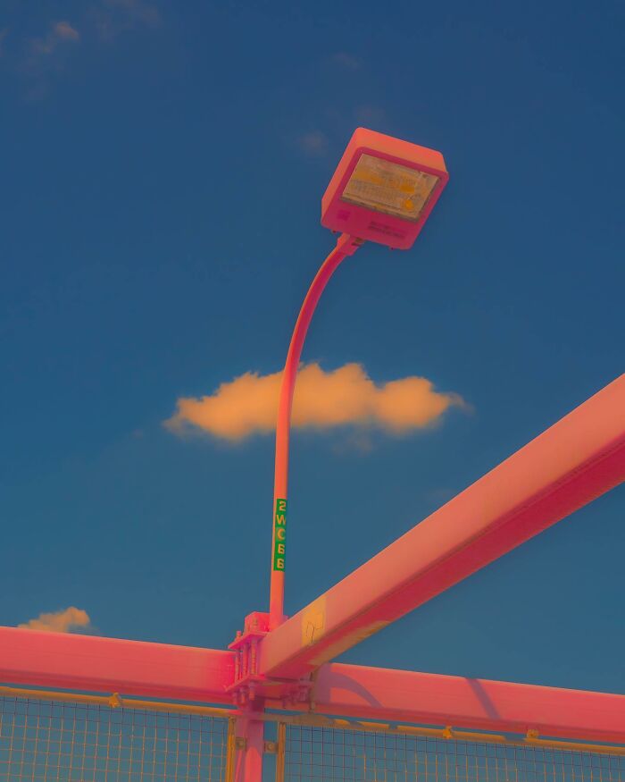 Street lamp and pink bridge structure against a deep blue sky with a single soft cloud in creative photo manipulations.