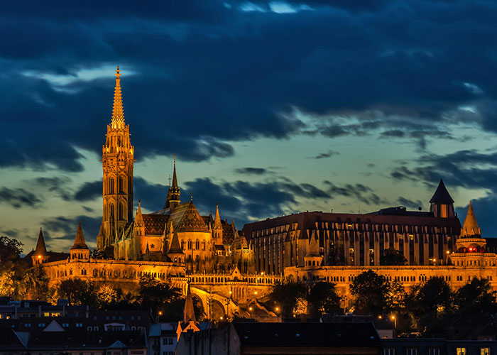 Night view of a historic European cityscape lit up under a dramatic sky, representing living in home countries.