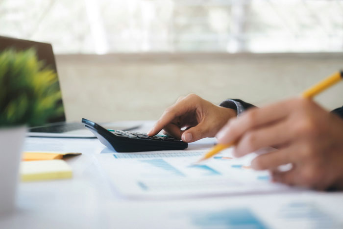 Person using calculator and pencil to analyze financial documents, illustrating common money saving mistakes that cost more.