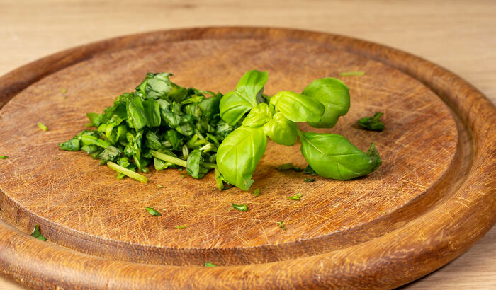 Chopped and whole fresh basil on a wooden cutting board, highlighting products requiring extra caution while cooking and eating.
