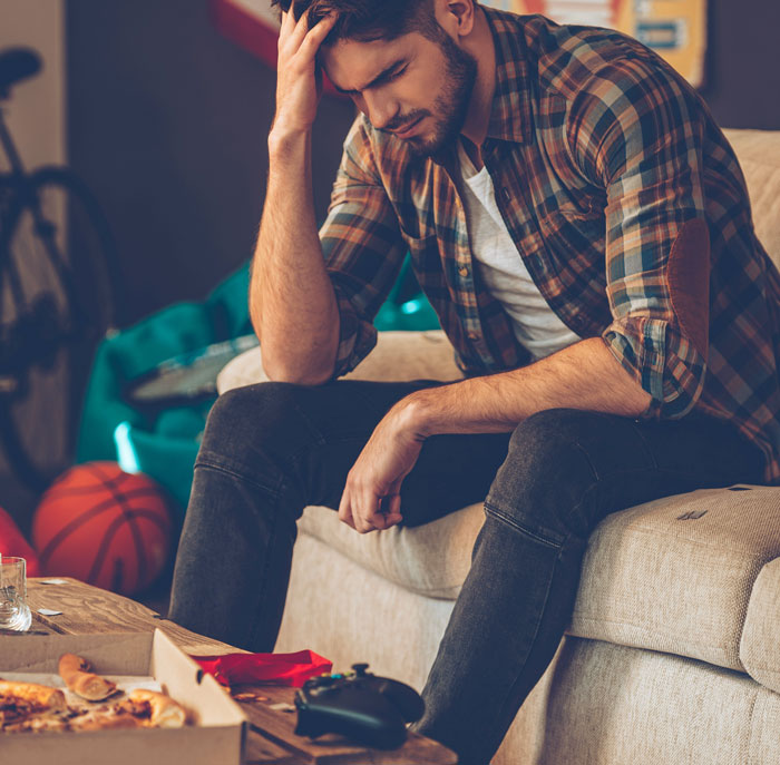 Young man sitting on couch looking stressed and anxious, symbolizing secrets spouses keep after marriage.