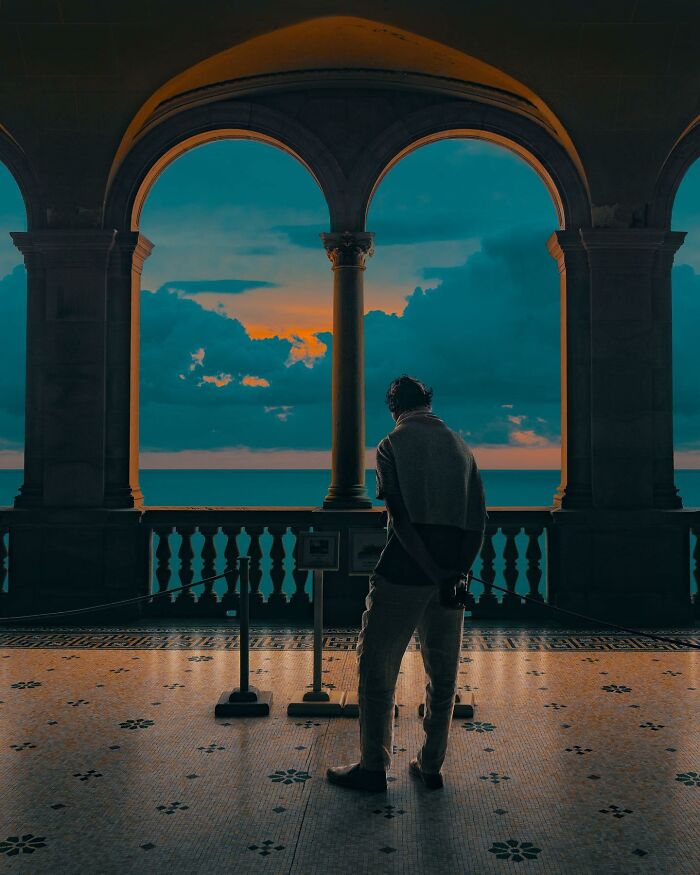 Person standing under arched stone windows overlooking ocean at sunset in a creative photo manipulation surreal reality scene.