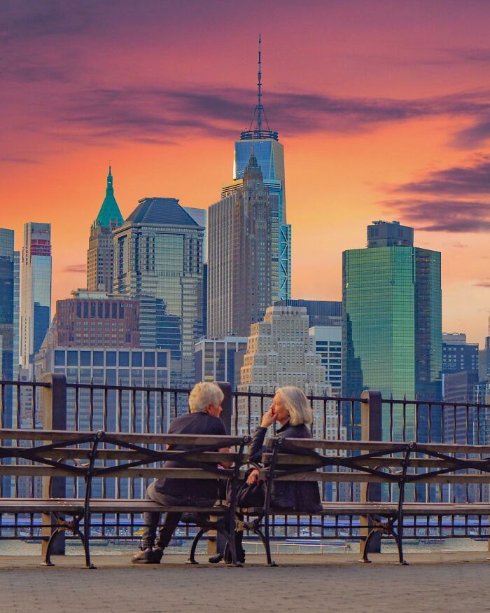 Couple sitting on a bench with a city skyline at sunset, showcasing creative photo manipulations and surreal reality elements.