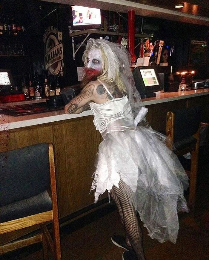Person in a tattered white dress and veil with smeared makeup sitting at a bar, a cursed image with eerie vibes.