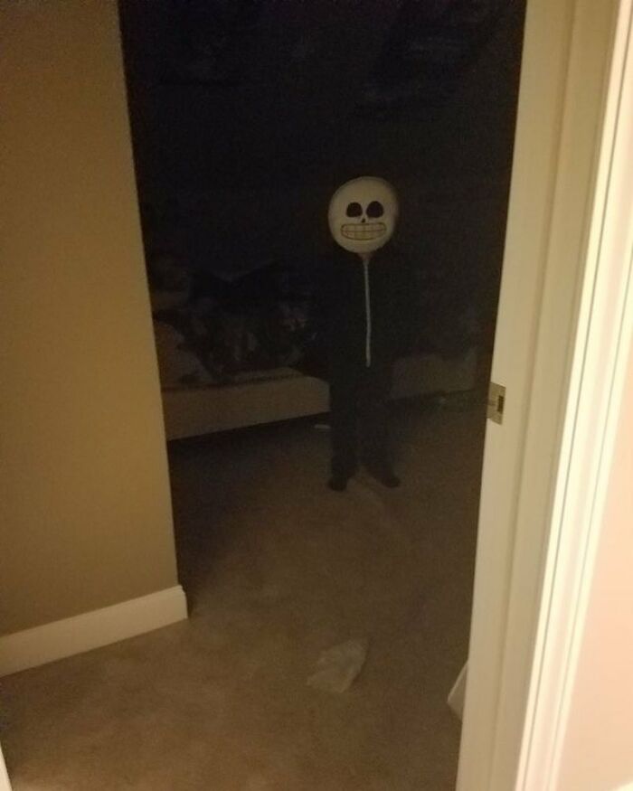 Child wearing a spooky skull mask standing in a dark room, a cursed image that gives a weird, unsettling vibe.