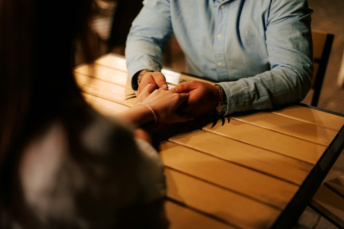 Woman holding roommate’s hands at a wooden table, expressing emotions about babysitting GF’s kids and doing the parent thing Woman holding roommate’s hands at a wooden table, expressing emotions about babysitting GF’s kids and doing the parent thing