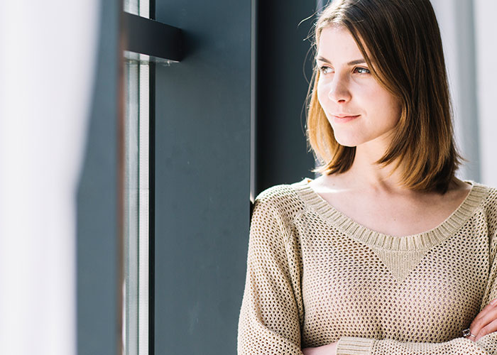 Woman standing by a window with arms crossed, reflecting on neighbor stealing packages and planning petty revenge. Woman standing by a window with arms crossed, reflecting on neighbor stealing packages and planning petty revenge.