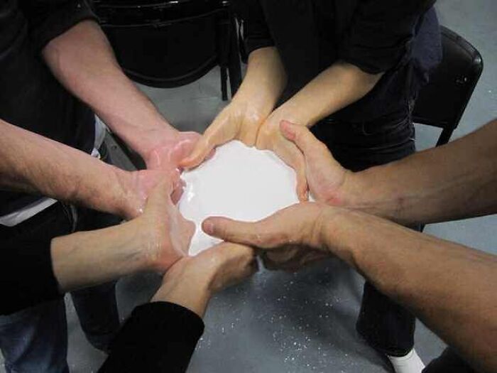 Several hands held together around a white liquid puddle, creating a weird cursed image effect for a strange break.