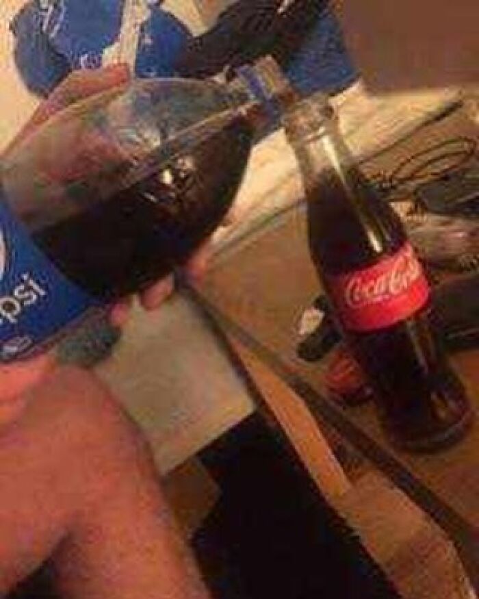 Person pouring Pepsi from a bottle into a classic glass Coca-Cola bottle, creating a cursed image of mixed sodas.