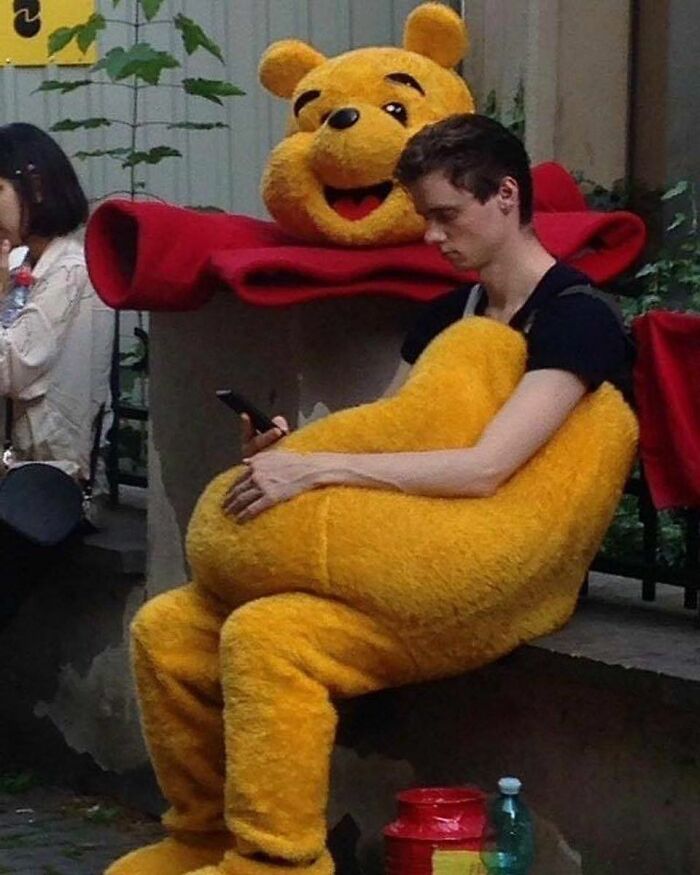 A person sitting in a partial Winnie the Pooh costume, holding the phone with the headpiece resting behind them in a cursed image.