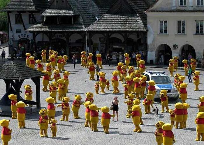 Dozens of people in Winnie the Pooh costumes clustered in a town square creating a cursed image effect.