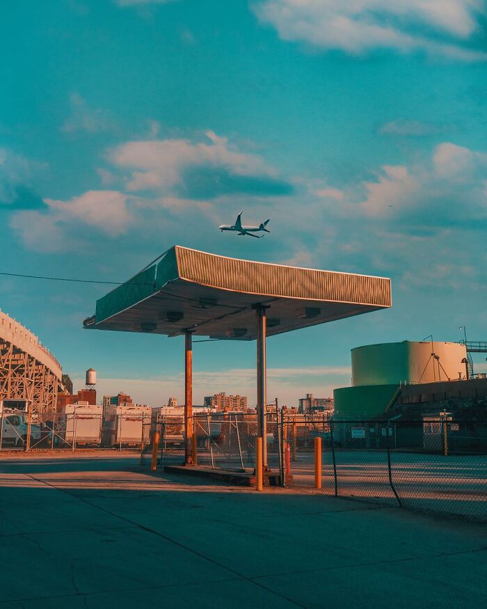 Surreal photo manipulation of an abandoned gas station with an airplane flying low under a vibrant sky.